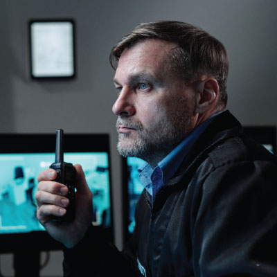Corrections office looking at monitors and holding a hand radio